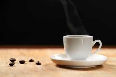 Kahve fincanı ve kahve çekirdekleri ahşap masada. Siyah arkaplan.