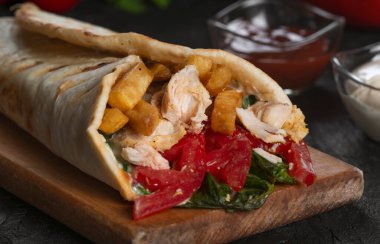 Shawarma sandviçi taze rulo, ızgara et ve siyah arka planda beyaz soslu salata..