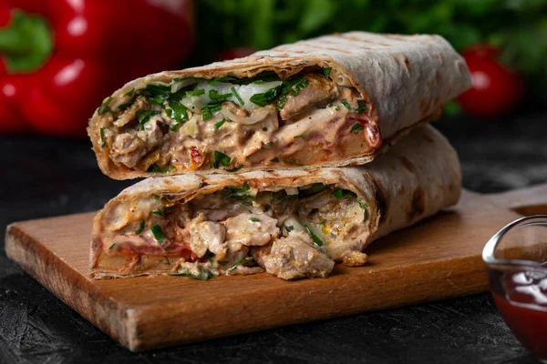 Shawarma sandviçi taze rulo, ızgara et ve siyah arka planda beyaz soslu salata..