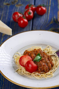 Beyaz tabakta spagetti bolonez makarna, tuz, biber, peynir ve domates mavi ahşap arka planda.