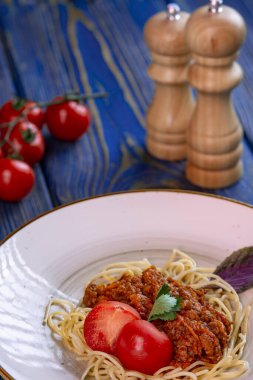 Kıymalı spagetti ve mavi ahşap arka planda vişneli domates..