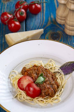 Etli makarna, domates sosu ve mavi ahşap masada sebzeler.