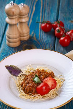 Kıymalı spagetti ve mavi ahşap arka planda vişneli domates..