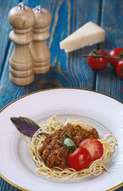 Etli makarna, domates sosu ve mavi ahşap masada sebzeler.