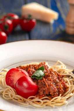 Beyaz tabakta spagetti bolonez makarna, tuz, biber, peynir ve domates mavi ahşap arka planda.