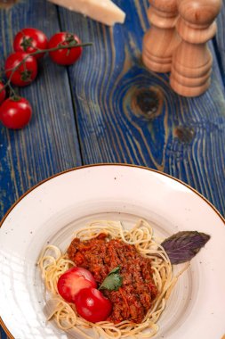 Kıymalı spagetti ve mavi ahşap arka planda vişneli domates..