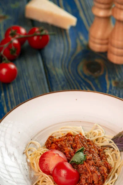 Mavi ahşap masada et, domates sosu ve sebzeli İtalyan makarnası bolonez. .