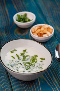 Yoğurt çorbası, mavi ahşap bir masada otlar ve krakerler.