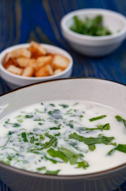 Yoğurt çorbası, mavi ahşap bir masada otlar ve krakerler.