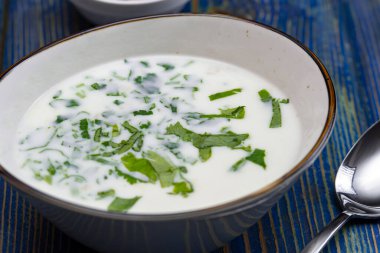 Yoğurt çorbası, mavi ahşap bir masada otlar ve krakerler.