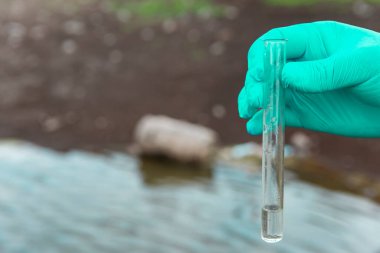 Analiz için nehirden örnek su. Bir test tüpü tutan eldiven. Ekoloji konsepti.