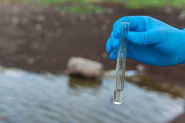 Analiz için nehirden örnek su. Bir test tüpü tutan eldiven. Ekoloji konsepti.