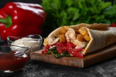 Shawarma sandviçi taze rulo, ızgara et ve siyah arka planda beyaz soslu salata..