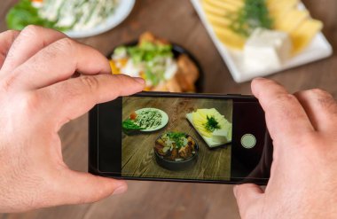 Gıda blogger fotoğraf çekmek akıllı telefon kullanarak . Mans eller geleneksel yemekler telefon fotoğrafçılığı yapmak. öğle yemeği ya da akşam yemeği et ve patates. Sosyal medya için, bloglama. En iyi görüntü cep telefonu.