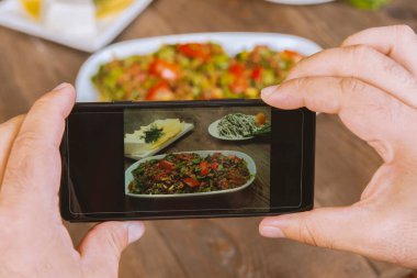 Yemek blogcusu akıllı telefon kullanarak fotoğraf çekiyor. Mans elleri geleneksel doğu yemeklerini telefonla çekiyor. Öğle ya da akşam yemeği. Sosyal medya ve blog için. Sağlıklı yemek.