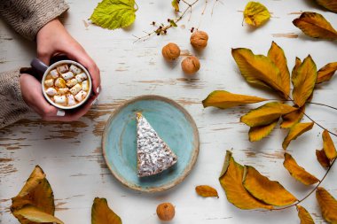 Pasta, ceviz ve saçılmış yapraklarla, sonbahar kompozisyonu eşliğinde eski püskü bir masada lokum tutan kadınların üst görüntüsü.
