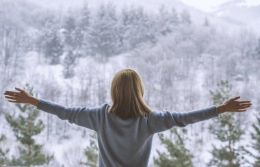 Kadın balkonda duruyor ve karlı dağlara bakıyor..