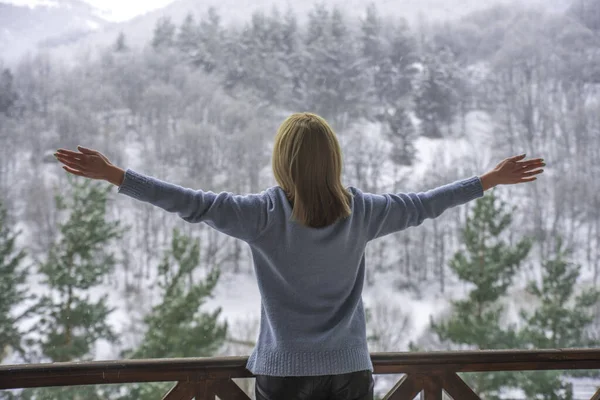 Kadın balkonda duruyor ve karlı dağlara bakıyor..