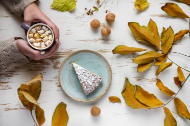 Pasta, ceviz ve saçılmış yapraklarla, sonbahar kompozisyonu eşliğinde eski püskü bir masada lokum tutan kadınların üst görüntüsü.