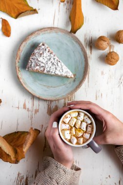 Pasta, ceviz ve saçılmış yapraklarla, sonbahar kompozisyonu eşliğinde eski püskü bir masada lokum tutan kadınların üst görüntüsü.