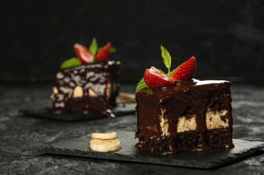 Çilekli çikolatalı pasta ve muz tabakta, siyah arka planda yakın plan.