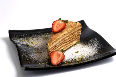 Beyaz arka planda izole edilmiş siyah bir tabakta çilekli katman sünger kek.