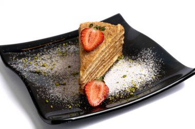 Beyaz arka planda izole edilmiş siyah bir tabakta çilekli katman sünger kek.