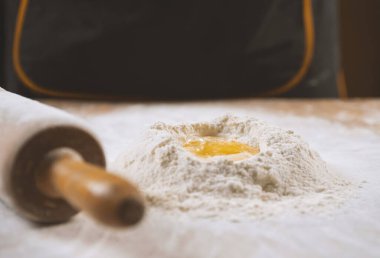 Yuvarlak bir iğne ve üzerinde yumurta sarısı olan un yığınlarının yakın çekimi.