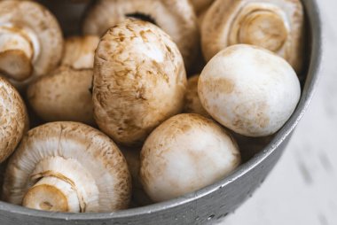 Beyaz ahşap arka planda demir bir kasede çiğ mantar.