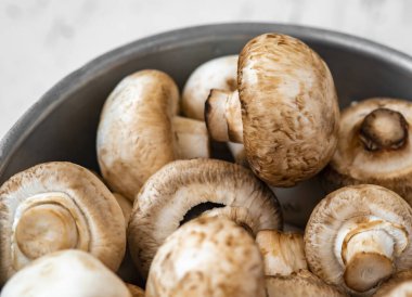 Beyaz ahşap arka planda demir bir kasede çiğ mantar.