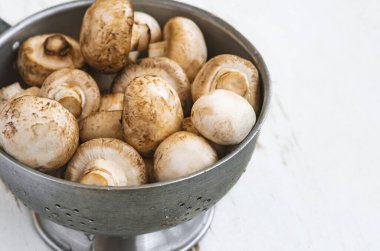 Beyaz ahşap arka planda demir bir kasede çiğ mantar.