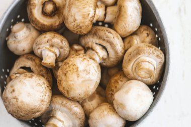 Beyaz ahşap arka planda demir bir kasede çiğ mantar.