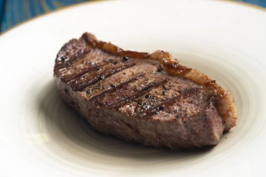 Taze ızgara et. Mavi ahşap arka planda beyaz tabakta baharatlı biftekler.