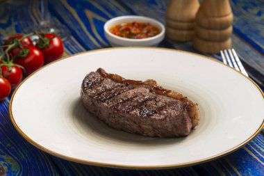 Kızarmış biftek, kiraz domatesleri, mavi ahşap masada tuz ve biber..
