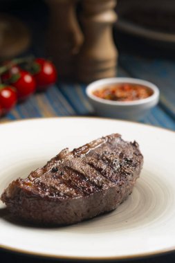 Kızarmış biftek, kiraz domatesleri, mavi ahşap masada tuz ve biber..