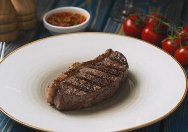 Kızarmış biftek, kiraz domatesleri, mavi ahşap masada tuz ve biber..