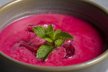 Cold beetroot soup with mint in a bowl on a gray background