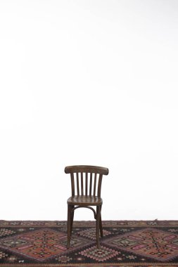 Beyaz arka planda, eski bir halının üzerinde tahta sandalye..