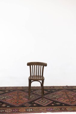 Beyaz arka planda, eski bir halının üzerinde tahta sandalye..