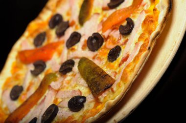 Jambonlu pizza, domates ve siyah arka planda zeytin.