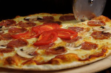 Tahtada jambon, peynir ve domatesle pizza kesme işlemi.