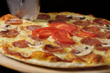 Tahtada jambon, peynir ve domatesle pizza kesme işlemi.