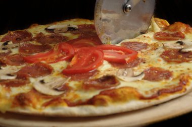 Tahtada jambon, peynir ve domatesle pizza kesme işlemi.