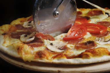 Tahtada jambon, peynir ve domatesle pizza kesme işlemi.