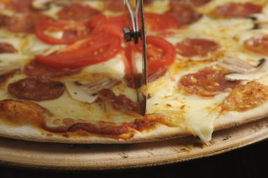 Tahtada jambon, peynir ve domatesle pizza kesme işlemi.