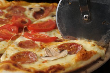 Tahtada jambon, peynir ve domatesle pizza kesme işlemi.