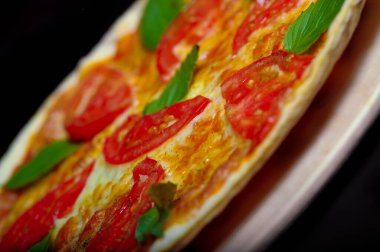 Domatesli pizza, mozarella ve siyah arka planda fesleğen.