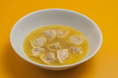 Sarı arka planda beyaz bir kasede çorba ile kaynatılmış hamur köftesi.