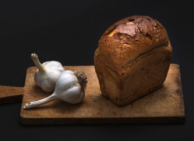 Karanlık ekmek ve siyah bir zemin üzerine sarımsak.