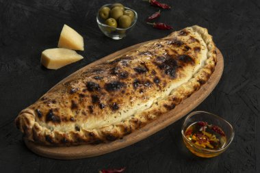 Siyah zemin üzerinde peynir ve zeytinli geleneksel calzone pizza..